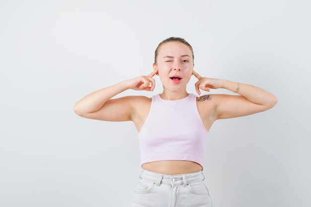 La femme blonde garde ses oreilles avec ses mains sur le fond blanc