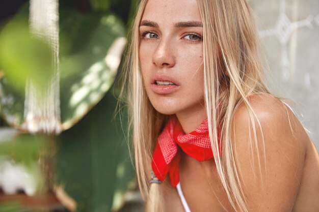 Femme blonde avec haut blanc et bandana rouge posant sur un café