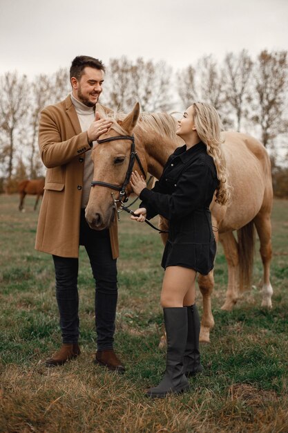 Femme blonde, homme brune debout sur le terrain avec un cheval brun. Femme portant des vêtements noirs et homme portant un manteau marron. Homme et femme touchant le cheval et parlant.