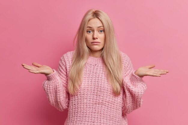 Une femme blonde incertaine se propage les paumes et se tient à l'intérieur du doute ne peut pas faire le choix entre deux options porte un pull chaud tricoté