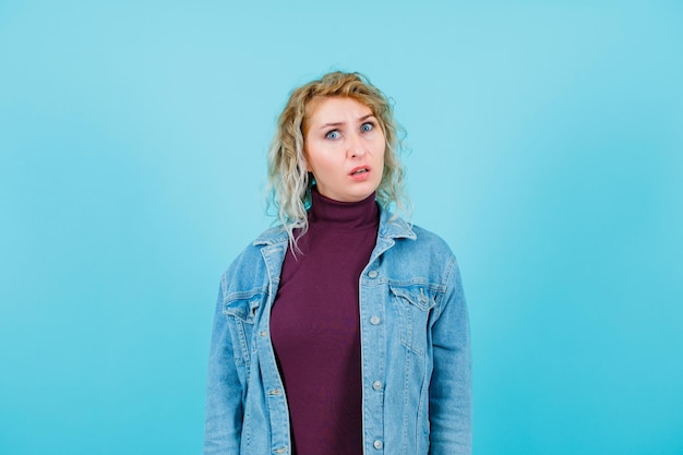 Une femme blonde insatisfaite regarde la caméra sur fond bleu