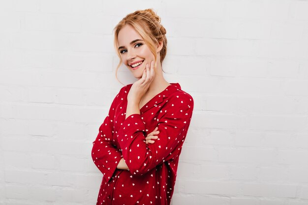 Femme blonde insouciante porte un pyjama lumineux souriant sur un mur blanc. Fille caucasienne à la mode profitant du matin du week-end.