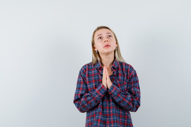 Femme blonde joignent les mains en geste de prière en chemise à carreaux et à la vue de face, focalisée.