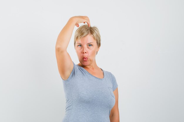 Femme blonde levant son bras au-dessus de la tête en t-shirt bleu clair et à la recherche concentrée. vue de face.