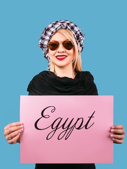 Femme blonde à lunettes de soleil et shemag arafatka avec table vide rose