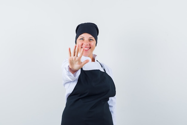 Photo gratuite femme blonde montrant le geste d'arrêt en uniforme de cuisinier noir et à la jolie.