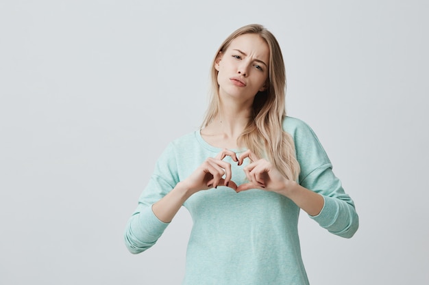 Femme Blonde Montrant Le Signe De L'amour Avec Ses Mains En Forme De Cœur. Belle Femme Européenne Habillée Avec Désinvolture Ressent L'amour. Romance Et Concept De Relations Humaines.