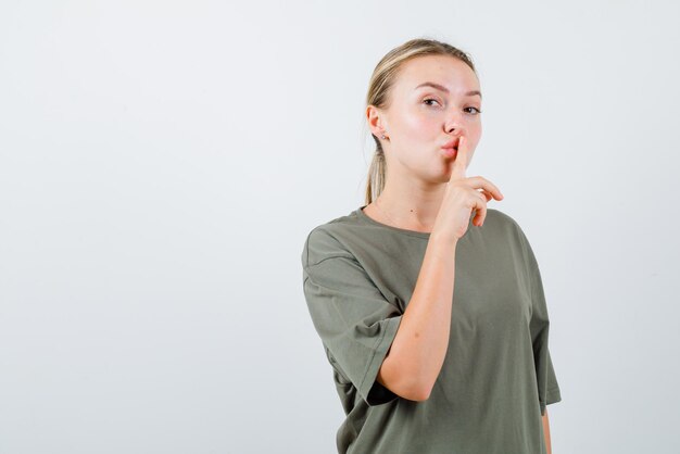 La femme blonde montre un geste silencieux en mettant l'index sur les lèvres sur fond blanc
