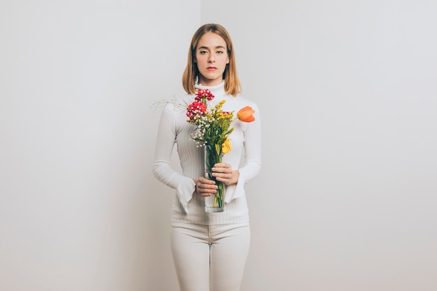 Femme blonde pensive avec des fleurs aux couleurs vives dans un vase