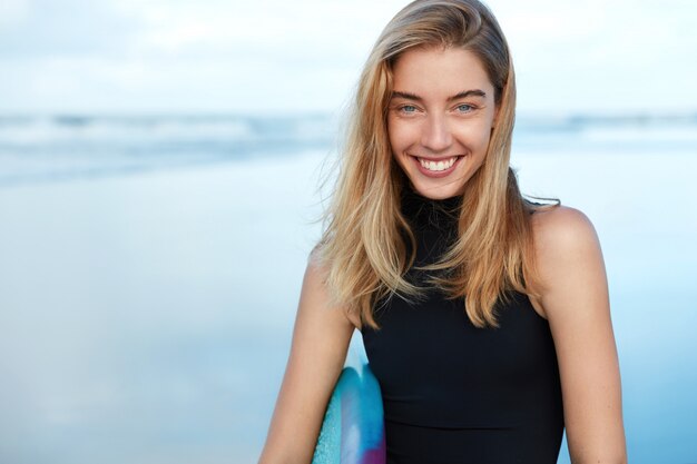 Femme blonde avec planche de surf sur la plage