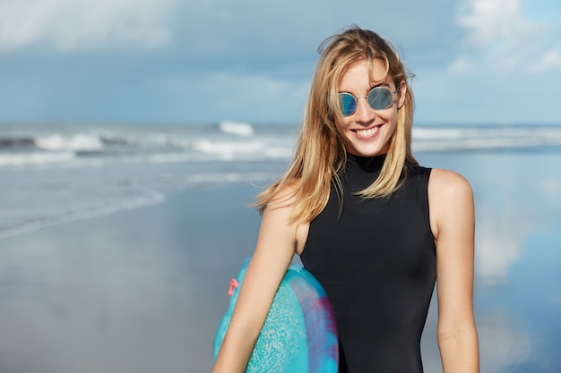 Femme blonde avec planche de surf sur la plage