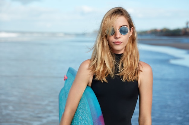 Femme blonde avec planche de surf sur la plage