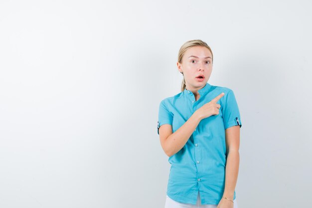 Femme blonde pointant vers le coin supérieur droit en blouse bleue isolée