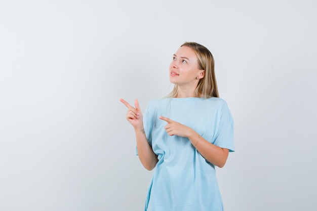 Femme blonde pointant vers la droite avec l'index en t-shirt bleu et à la mignonne