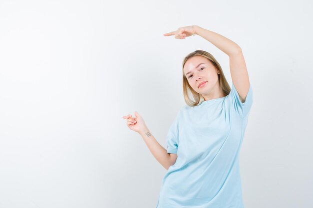 Femme blonde pointant vers la gauche avec l'index en t-shirt bleu et l'air heureux