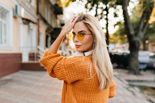 Femme blonde en pull tricoté marron regardant par-dessus l'épaule avec joli sourire