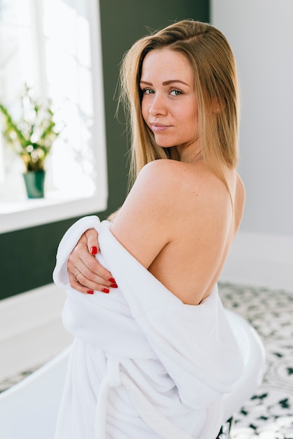 Photo gratuite femme blonde qui pose dans la salle de bain avec un peignoir