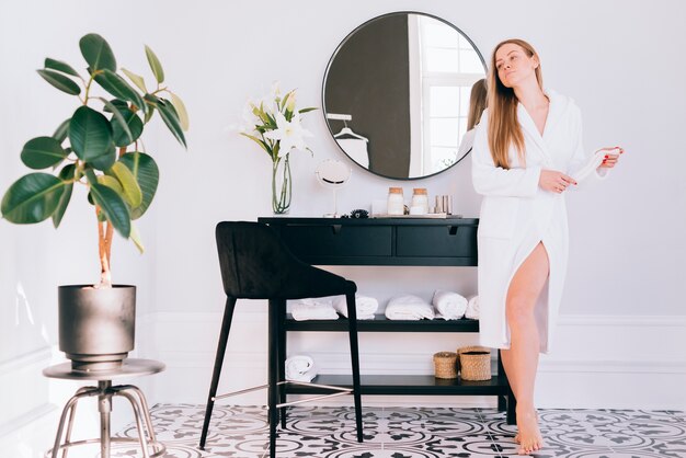 Femme blonde qui pose dans la salle de bain avec un peignoir