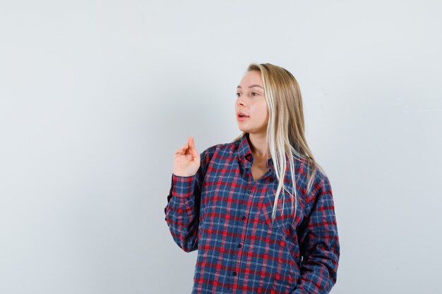 Femme blonde qui s'étend d'une main tout en parlant à quelqu'un en chemise à carreaux et à la vue de face, focalisée.