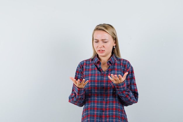 Femme blonde regardant étonnamment les mains en chemise à carreaux et à la surprise, vue de face.