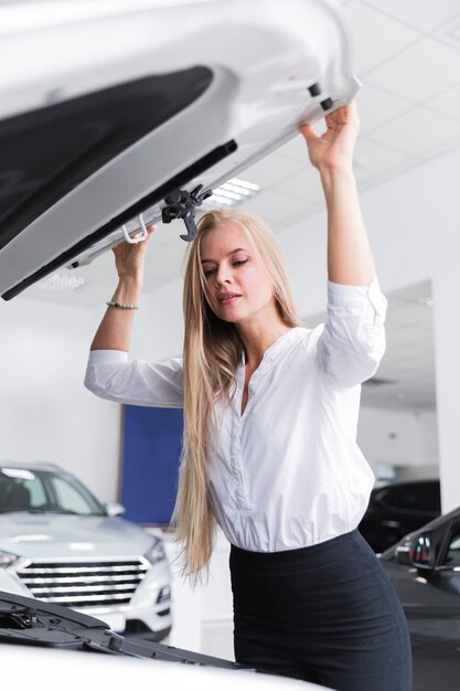 Femme blonde regardant sous le capot de la voiture