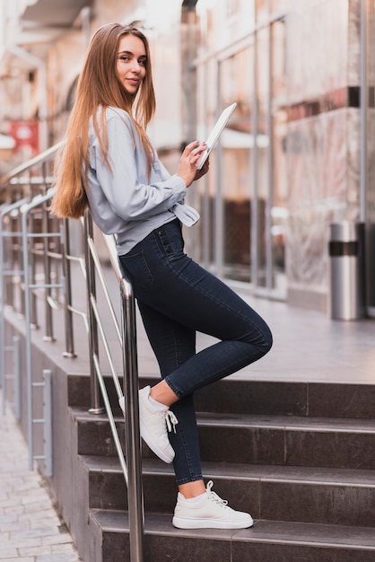 Femme blonde reposant sur une balustrade et tenant une tablette