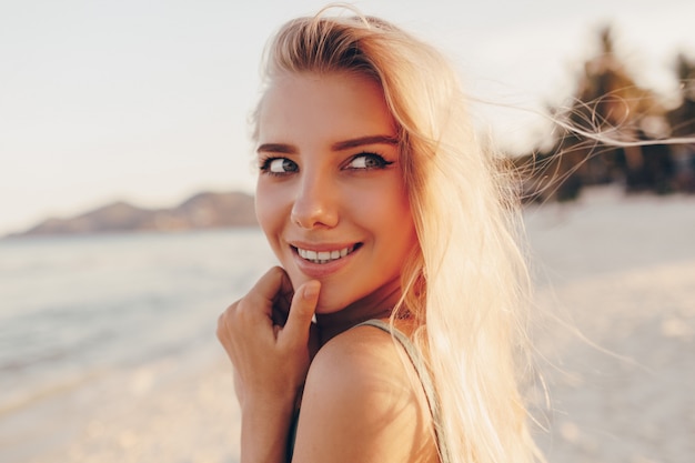 Femme blonde rêveuse posant sur la plage