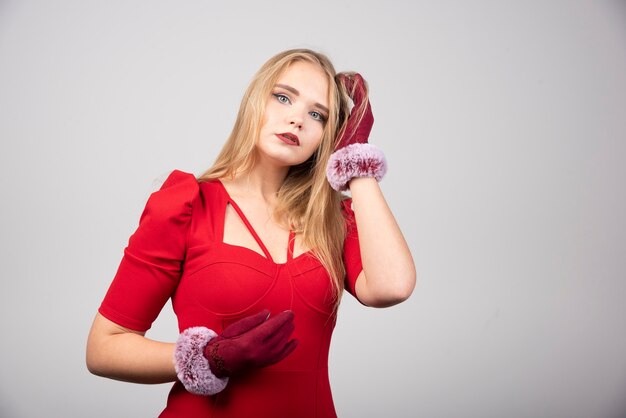 Femme blonde en robe de cocktail rouge debout sur fond gris.