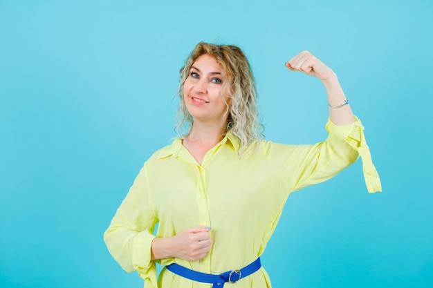 Une femme blonde souriante lève le poing sur fond bleu