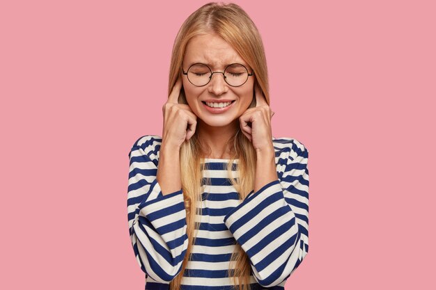 Une femme blonde stressante se bouche les oreilles, fait la grimace, ignore le son désagréable