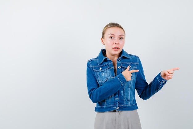 La femme blonde surprise pointe vers la droite avec des avant-bras sur fond blanc