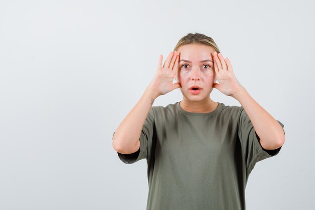 La femme blonde surprise tient ses mains face à face sur fond blanc