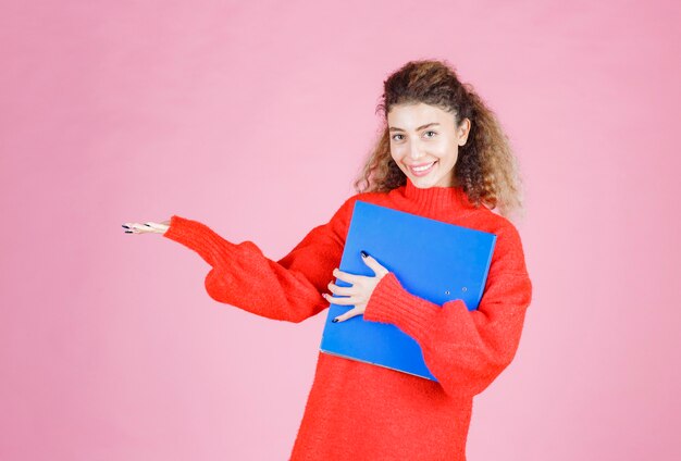 Femme blonde en sweat rouge pointant quelque part sur le côté gauche.