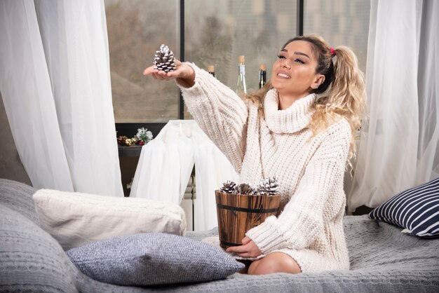 Femme blonde en sweat-shirt blanc offrant des pommes de pin.