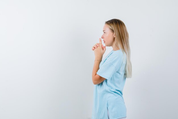 Femme blonde en t-shirt bleu montrant le geste du pistolet devant la bouche et l'air confiant