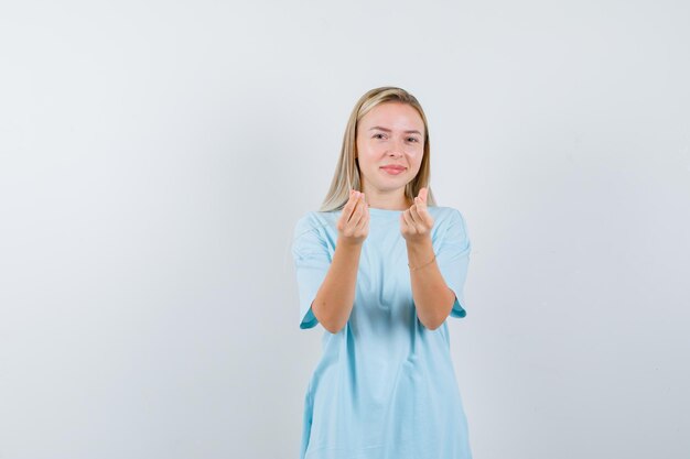 Femme blonde en t-shirt bleu montrant un geste italien et semblant mignonne