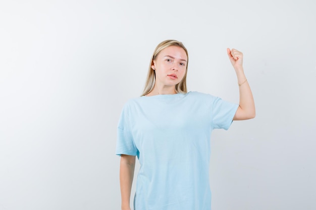 Femme blonde en t-shirt bleu montrant les muscles et l'air confiant