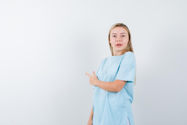 Femme blonde en t-shirt bleu pointant vers la gauche avec l'index et à la surprise