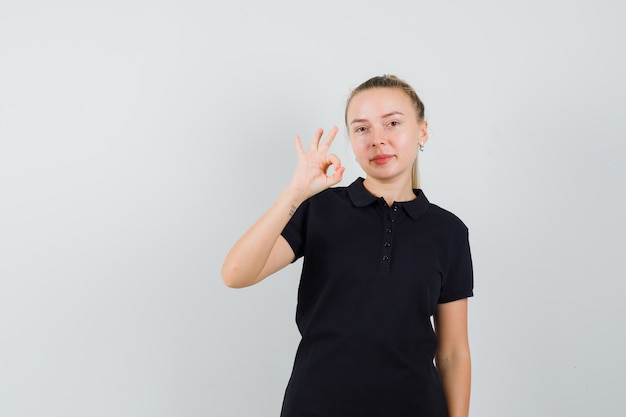 Femme blonde en t-shirt noir montrant le signe ok et l'air heureux