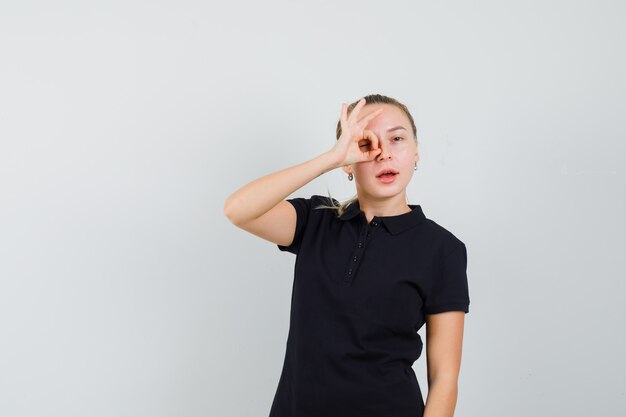 Femme blonde en t-shirt noir montrant le signe ok et à l'optimiste