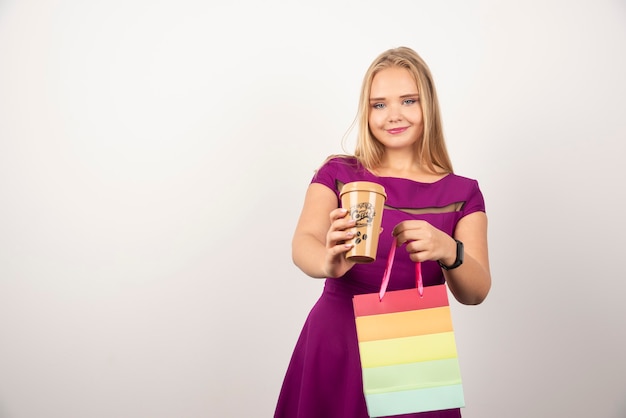 Femme blonde avec une tasse de café et un sac posant.