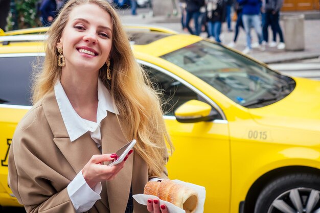 Une femme blonde avec un téléphone dans une rue d'une ville européenne mangeant du trdlo à praha.