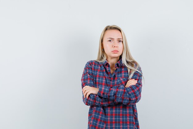 Femme blonde tenant les bras croisés en chemise à carreaux et à la grave, vue de face.