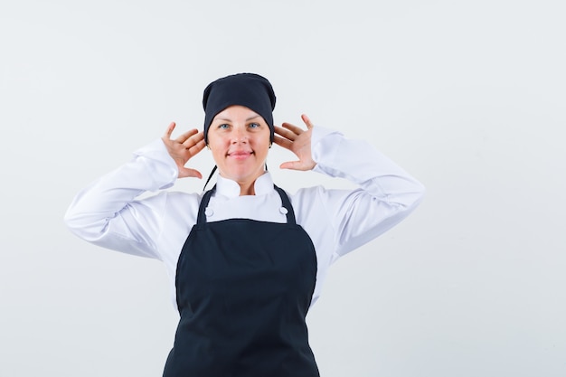 Femme Blonde Tenant La Main Près De L'oreille En Uniforme De Cuisinier Noir Et à La Jolie Vue De Face.