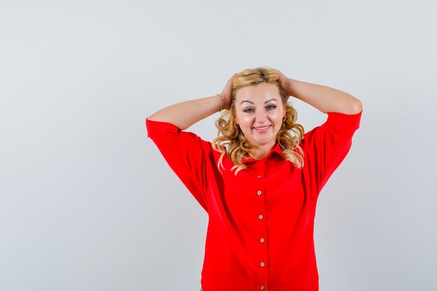 Femme blonde tenant les mains sur la tête en chemisier rouge et à la recherche de bonheur.