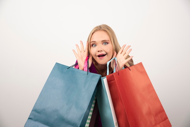 Femme blonde tenant des sacs à provisions avec une expression heureuse.