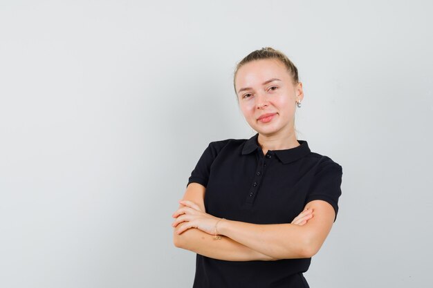 Femme blonde tenant ses bras croisés et souriant en t-shirt noir