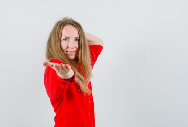 Femme blonde tendant la main et souriant en chemise rouge