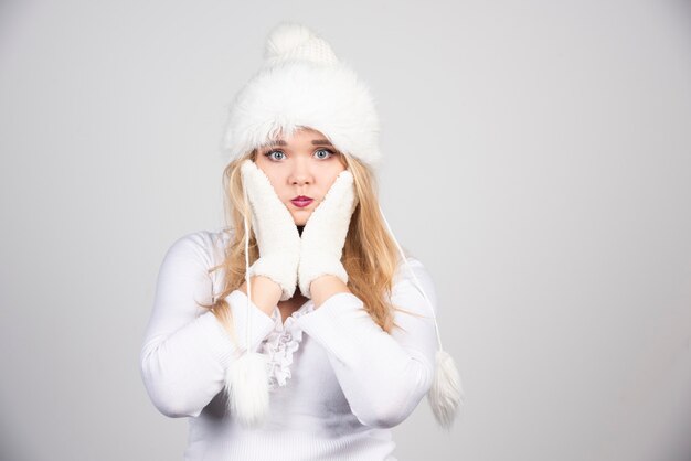 Femme blonde en tenue d'hiver tenant son visage.