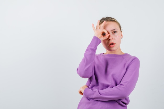 La femme blonde tient ses doigts autour des yeux sur fond blanc